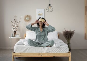 woman with eye mask sitting in bed smiling