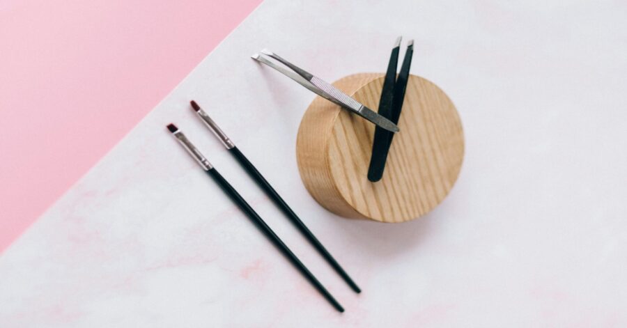 Tweezers and Makeup Brushes on Pink Surface